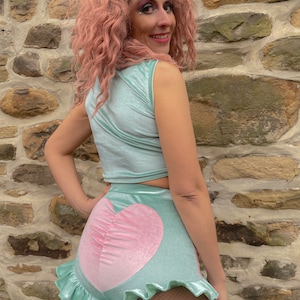 May include: A light blue velvet crop top and matching shorts with a pink heart design. The shorts have a ruffled hem.