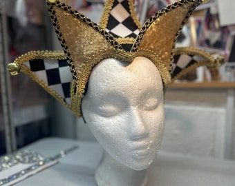 May include: A black and white checkered jester hat with gold sequins and trim. The hat has bells on the points and is worn on a white mannequin head.