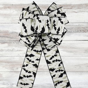 Può includere: Un grande fiocco decorativo a tema Halloween. Il fiocco è bianco con un motivo di pipistrelli neri. I bordi sono rifiniti con un bordo nero. Il fiocco è realizzato in tessuto ed è adatto per decorare ghirlande, regali o altri lavori creativi.