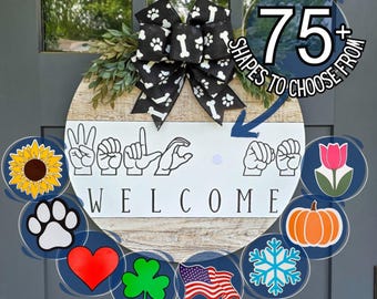 May include: A round wooden welcome sign with a black and white bow featuring paw prints and bones. The sign spells "Welcome" in American Sign Language. Includes various decorative shapes like a sunflower, paw print, heart, and flag.