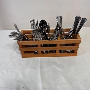 May include: A wooden cutlery organizer filled with various stainless steel forks, spoons, and knives. The organizer has a rectangular shape with multiple compartments. The utensils are arranged neatly inside, ready for use.