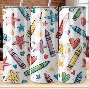 May include: Three white insulated tumblers with a colorful pattern of crayons, stars, and hearts. The design features red, blue, yellow, green, and purple crayons, along with various star and heart shapes. Each tumbler has a white straw.