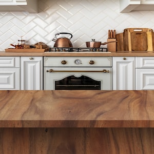 May include: A wooden countertop with a white kitchen in the background. The kitchen features white cabinets, a white tiled backsplash, and a white stove with a brass oven door.