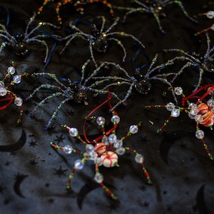 May include: A collection of beaded spider ornaments with red and white candy cane-like bodies. The spiders are made with iridescent beads and have long legs.