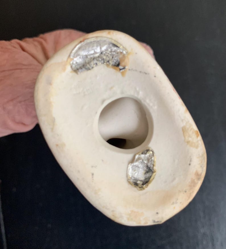 Peut inclure: Le dessous d'une figurine en c&eacute;ramique blanche avec un trou au centre. Il y a deux autocollants argent&eacute;s sur le fond de la figurine.