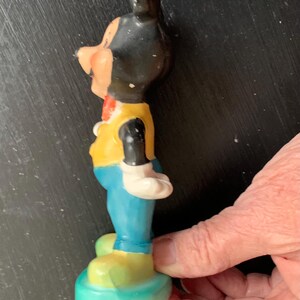 Peut inclure: Une figurine en c&eacute;ramique vintage de Mickey Mouse portant un gilet jaune, un pantalon bleu et des chaussures jaunes. La figurine est debout sur une base bleue.