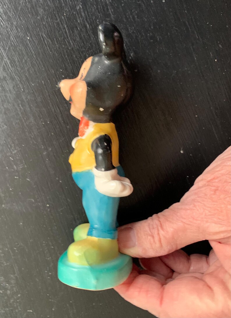 Peut inclure: Une figurine en c&eacute;ramique vintage de Mickey Mouse portant un gilet jaune, un pantalon bleu et des chaussures jaunes. La figurine est debout sur une base bleue.