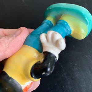 Peut inclure: Une figurine en c&eacute;ramique d'un personnage de dessin anim&eacute; portant un pantalon bleu, une chemise jaune et des gants blancs. Le personnage a des chaussures noires et un visage noir.