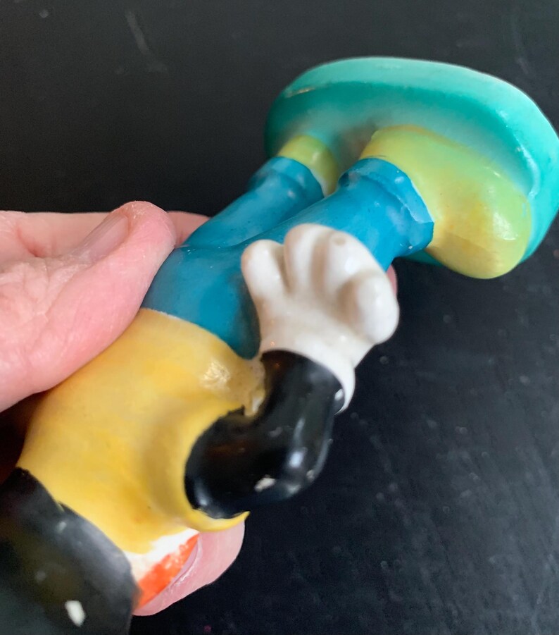 Peut inclure: Une figurine en c&eacute;ramique d'un personnage de dessin anim&eacute; portant un pantalon bleu, une chemise jaune et des gants blancs. Le personnage a des chaussures noires et un visage noir.