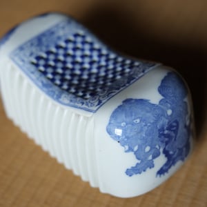以下が含まれることがあります： 青と白のパターンで装飾された白いセラミック枕。枕は隆起した質感のある表面を持ち、スタイリッシュなライオンのデザインが特徴です。