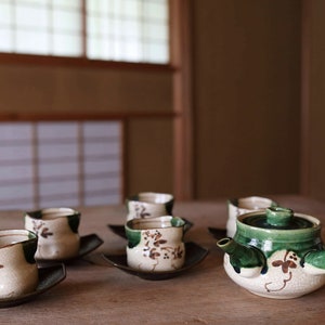 May include: A traditional Japanese tea set with a green and white teapot and four matching cups. The set is made of ceramic and features a floral design.