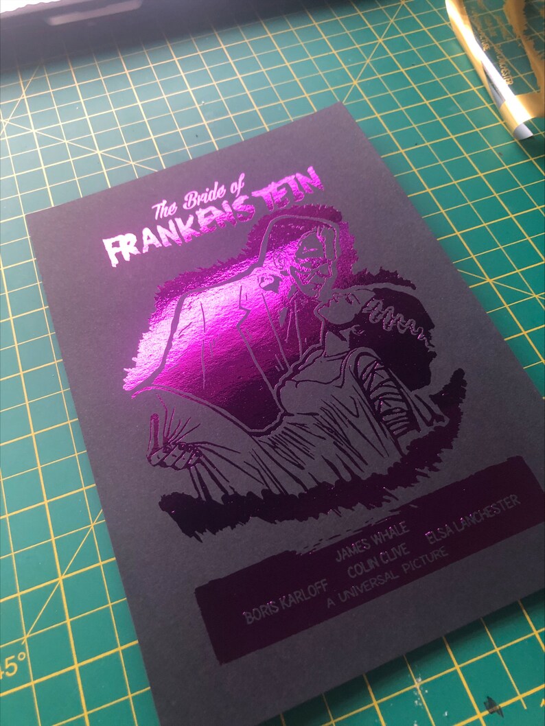 K&ouml;nnte beinhalten: Ein schwarz-wei&szlig;es Poster mit einer pinkfarbenen Folien&uuml;berlagerung. Das Poster zeigt eine schwarz-wei&szlig;e Illustration eines Monsters aus dem Film "Die Braut des Frankenstein". Der Text auf dem Poster lautet "Die Braut des Frankenstein", "Boris Karloff", "James Whale", "Colin Clive", "Elsa Lanchester" und "Ein Universal-Film".