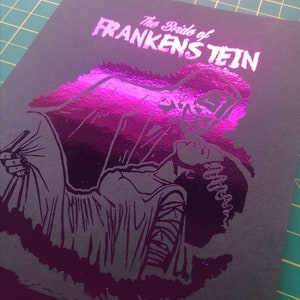 K&ouml;nnte beinhalten: Ein schwarz-wei&szlig;es Poster mit einem pinkfarbenen Foliendruck eines Monsters aus dem Film "Die Braut des Frankenstein". Das Poster zeigt den Text "Die Braut des Frankenstein" und die Namen "James Whale" und "Colin Clive".