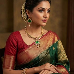 May include: A woman wearing a traditional Indian sari in shades of green, red, and gold. She is adorned with gold jewelry, including a necklace, earrings, bangles, and a ring. Her hair is styled with flowers.