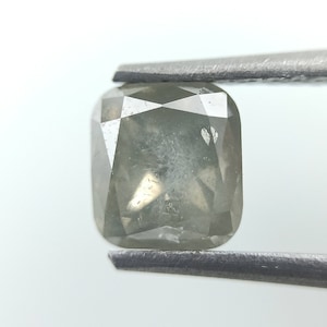 Op de afbeelding: Een lichtgrijze, kussen geslepen diamant met een troebele, ondoorzichtige uitstraling. De diamant wordt vastgehouden door een pincet.