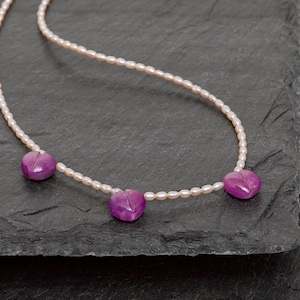 Op de afbeelding: Een roze parelketting met drie roze hartvormige edelstenen.