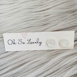 May include: A pair of white iridescent round stud earrings on a white card with the text "Oh So Lovely" printed on it.