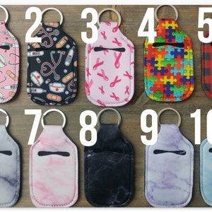 May include: Ten different designs of hand sanitizer holders with keychains. The holders are made of a soft, flexible material and have a clear window for easy access to the sanitizer. The designs include a nurse theme, pink ribbons, puzzle pieces, plaid, marble, and more.