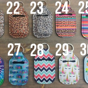 May include: Ten colorful hand sanitizer holders with keychains. The holders are made of fabric and have various patterns, including animal print, tie-dye, and geometric designs. Each holder is numbered from 21 to 30.
