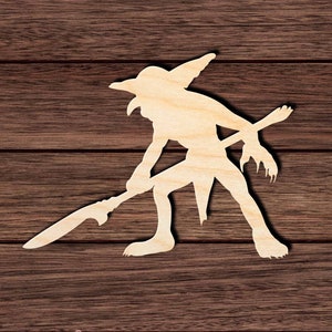 May include: A wooden cutout of a goblin holding a spear. The goblin is standing with its legs spread apart and its arms outstretched. The cutout is made of light brown wood and has a smooth finish.