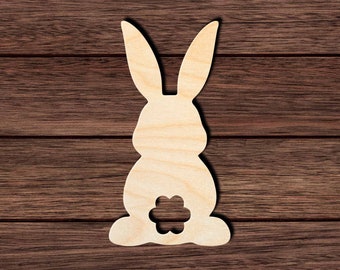 May include: A wooden cutout of a bunny rabbit with a flower shape cut out of its rear end. The bunny is facing forward with its ears up.