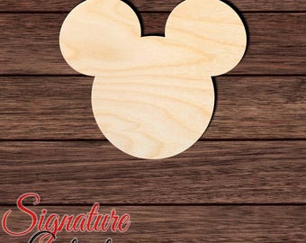 May include: A light-colored, unfinished wooden cutout in the shape of a mouse head with two circular ears and a larger circular face. The surface shows natural wood grain patterns. The text Signature Cutouts is visible in the bottom left corner.