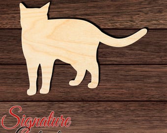 May include: A light-colored, flat wooden cutout in the shape of a standing cat viewed from the side. The cat silhouette features pointed ears, a smooth body outline, and a long, slightly curved tail extending to the right side of the frame.