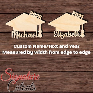 May include: Two wooden graduation cap cutouts with the names "Michael" and "Elizabeth" and the years "2026" and "2021" written on them. The cutouts are on a woodgrain background.