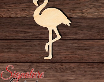 May include: A light-colored wooden cutout in the shape of a flamingo standing on one leg with its neck curved. The cutout features a smooth, natural wood grain finish and is positioned against a dark brown horizontal wood plank background.