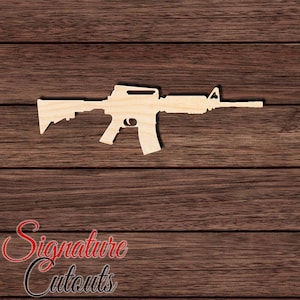 May include: A light-colored, flat wooden cutout shaped like an AR-15 style rifle. The silhouette features a distinct stock, a pistol grip, a magazine, a handguard, and a front sight post, all rendered in a smooth, unfinished natural wood grain texture.