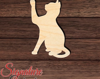 May include: A light-colored wooden cutout in the shape of a sitting cat with one front paw raised. The cat silhouette features smooth edges and a natural wood grain texture. The text Signature Cutouts is visible in the bottom left corner.