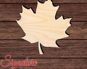 May include: A light-colored wooden cutout in the shape of a maple leaf with a smooth surface and visible natural wood grain patterns. The leaf features a central stem at the bottom and multiple pointed lobes characteristic of a maple leaf silhouette.