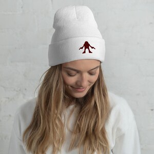 May include: White beanie with a red embroidered monster design. The beanie is made of a soft, comfortable material and is perfect for keeping warm in the winter.