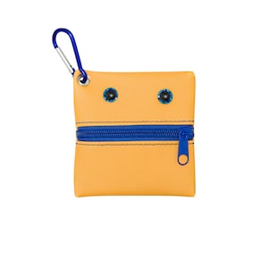 May include: A small yellow zippered pouch with a blue zipper and two blue eyes. The pouch has a silver clip attached to the top.