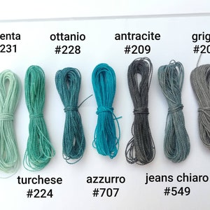 K&ouml;nnte beinhalten: Eine Sammlung von acht Spulen Baumwollschnur in verschiedenen Blaut&ouml;nen, Gr&uuml;nt&ouml;nen und Graut&ouml;nen. Die Spulen sind mit italienischen Namen und Farbcodes beschriftet, wie z. B. "menta #231", "ottanio #228", "antracite #209", "grigio #206", "turchese #224", "azzurro #707" und "jeans chiaro #549".