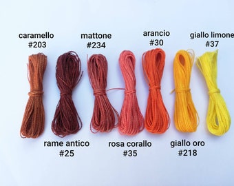 Op de afbeelding: Een verzameling kleurrijke katoenen koorden, gerangschikt in een rij. De koorden zijn gelabeld met Italiaanse namen en kleurcodes, zoals "caramello #203", "mattone #234", "arancio #30", "giallo limone #37", "rame antico #25", "rosa corallo #35" en "giallo oro #218".