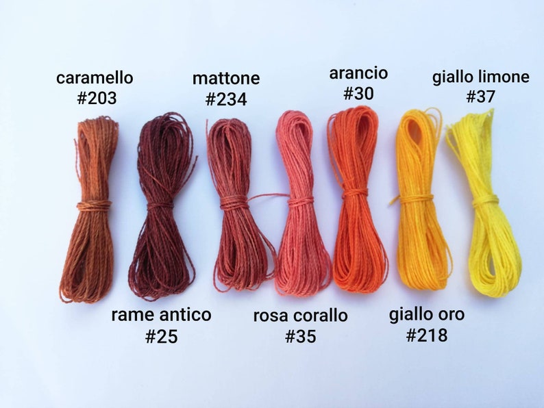 K&ouml;nnte beinhalten: Eine Sammlung bunter Baumwollschn&uuml;re, die in einer Reihe angeordnet sind. Die Schn&uuml;re sind mit italienischen Namen und Farbcodes beschriftet, wie z. B. "caramello #203", "mattone #234", "arancio #30", "giallo limone #37", "rame antico #25", "rosa corallo #35" und "giallo oro #218".