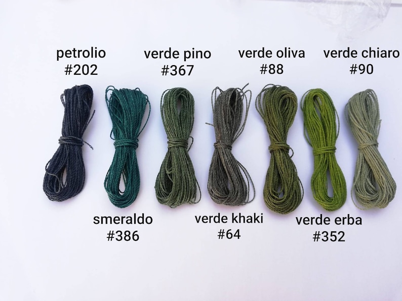 K&ouml;nnte beinhalten: Acht Garnrollen in verschiedenen Gr&uuml;nt&ouml;nen und Blau. Die Rollen sind mit italienischen Namen und Nummern beschriftet, wie "petrolio #202", "verde pino #367", "verde oliva #88", "verde chiaro #90", "smeraldo #386", "verde khaki #64" und "verde erba #352".