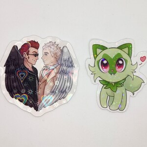 May include: Two cartoon characters, one with black wings and the other with white wings, are standing side-by-side. They are both smiling and looking at each other. The background is a heart shape with rainbow hearts and stars. A green cartoon character with big eyes and a heart above its head is also shown.