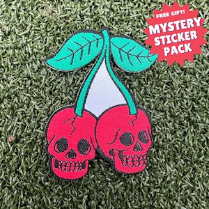 Könnte beinhalten: Zwei rote Kirschen mit Totenkopfgesichtern, einem grünen Stiel und Blättern. Die Kirschen befinden sich auf grünem Hintergrund. GRATIS GESCHENK! MYSTERY STICKER PACK.