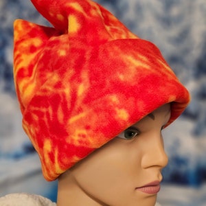 May include: A red and yellow fleece hat with a pointed top. The hat is worn by a mannequin with a neutral expression.