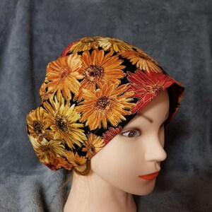 May include: A black fabric hat with a floral print of orange, yellow, and red flowers. The hat is worn on a mannequin head.