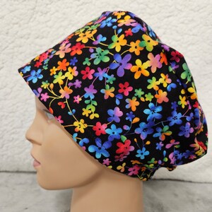 May include: A black scrub hat with a colorful floral print. The flowers are in shades of pink, blue, green, yellow, and orange. The hat has a gathered back and a tie at the back.