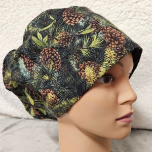 May include: A black scrub hat with a pine cone and evergreen print. The hat is made of a soft, comfortable fabric and has a tie at the back.