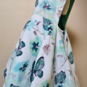 May include: A white hooded fleece cape with a butterfly and floral print in shades of green, blue, and pink.