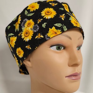 May include: Black scrub hat with a sunflower and bee print. The hat has a tie at the back.