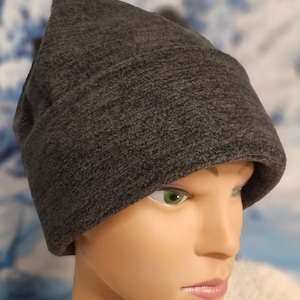 May include: A gray fleece beanie with a pointed top. The beanie is made of a soft, textured fabric.