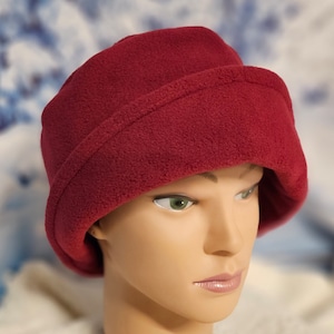May include: A burgundy fleece hat with a wide brim. The hat is folded down in the front and has a seam around the brim.