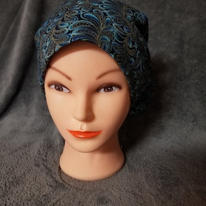May include: A blue and gold patterned beanie hat with a swirl design.