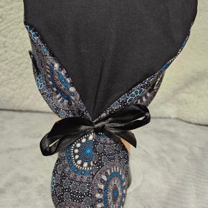 May include: A black scrub hat with a patterned tie. The tie is made of a fabric with a blue, white, and gray pattern of circles and dots. The hat is tied with a black ribbon.